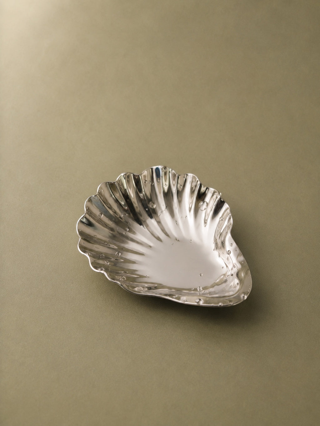 Studio Boy Shell stainless steel serving plate with a polished finish and seashell shape on a neutral background.